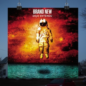 May include: Poster featuring an astronaut in a gold spacesuit against a fiery red and orange background. The poster has the text "BRAND NEW" and "DEJA ENTENDU" in white lettering. The astronaut appears to be floating above a teal body of water.