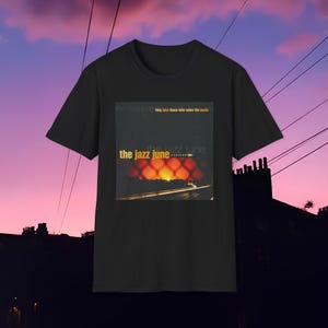 Op de afbeelding: Zwart T-shirt met een afbeelding van een zonsondergang boven een snelweg met de tekst "the jazz june" en het citaat "they love those who make the music".