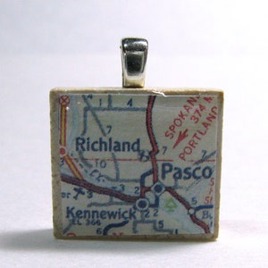 May include: A beige ceramic pendant with a map of the Tri-Cities area of Washington state. The map shows the cities of Richland, Kennewick, and Pasco. The pendant has a silver bail.