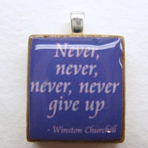 Puede incluir: Un colgante cuadrado con fondo azul y texto blanco que dice "Never, never, never, never give up - Winston Churchill". El colgante est&aacute; hecho de madera y tiene una anilla de plata.