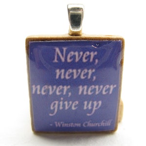 Puede incluir: Un peque&ntilde;o colgante cuadrado con una anilla de plata. El colgante est&aacute; hecho de un material marr&oacute;n claro y tiene un fondo azul con una cita blanca que dice "Never, never, never, never give up - Winston Churchill".