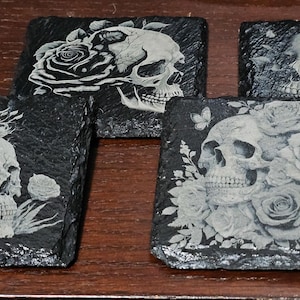 May include: Set of four black slate coasters with white engraved images of skulls and roses.