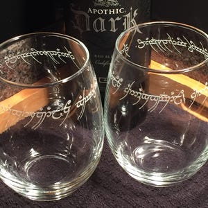 May include: Two clear glass wine glasses with the inscription "One Ring to rule them all, One Ring to find them, One Ring to bring them all and in the darkness bind them" etched around the top of each glass.