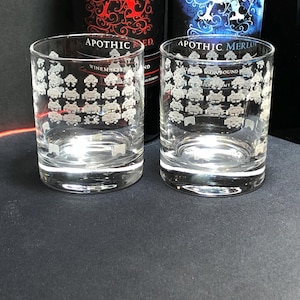 Puede incluir: Dos vasos transparentes de vidrio con un diseño blanco de invasores espaciales. Los vasos están sobre una superficie negra. El texto en los vasos dice "Apothic Red" y "Apothic Merlot".