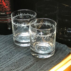 May include: Four clear glass tumblers with the inscription "One Ring to rule them all" etched on the side. The inscription is in the Elvish language from the Lord of the Rings.