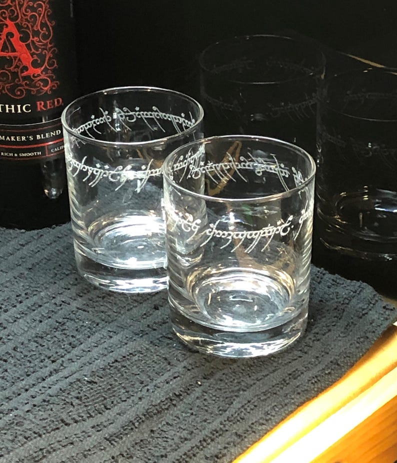 May include: Four clear glass tumblers with the inscription "One Ring to rule them all" etched on the side. The inscription is in the Elvish language from the Lord of the Rings.