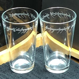 May include: Two clear glass pint glasses with the inscription "One Ring to rule them all, One Ring to find them, One Ring to bring them all and in the darkness bind them" etched around the top.