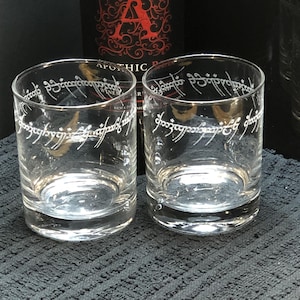 Op de afbeelding: Twee heldere glazen tumblers met de inscriptie "Een Ring om ze te regeren, Een Ring om ze te vinden, Een Ring om ze allen te brengen en in de duisternis te binden" gegraveerd rond de bovenkant.