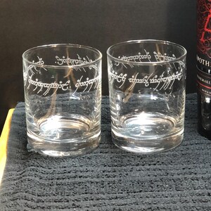 May include: Two clear glass tumblers with the inscription "One Ring to rule them all" etched on the side. The inscription is in the Elvish language from the Lord of the Rings.
