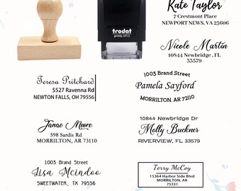 May include: A wooden address stamp with a light brown handle and a rectangular base, next to a black self-inking stamp. Several examples of printed addresses are displayed, including names and street addresses.