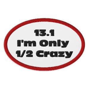 May include: Embroidered patch with a white oval center and a red border. The patch features the text "13.1 I'm Only 1/2 Crazy" in black, stitched lettering. This patch is likely for a marathon or half-marathon runner.