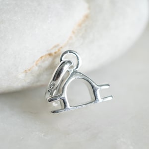 May include: Silver charm in the shape of the Libra zodiac sign. The charm has a loop at the top for attaching to a bracelet or necklace. The charm is marked with "925" on the back.