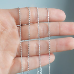May include: Four silver chains of varying lengths, displayed on a hand.