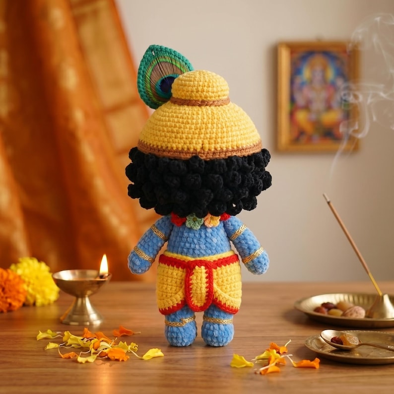 Puede incluir: Mu&ntilde;eca de ganchillo hecha a mano de una deidad, con un sombrero amarillo y una pluma de pavo real, cabello negro y ropa azul y amarilla. La mu&ntilde;eca est&aacute; colocada sobre una superficie de madera con una peque&ntilde;a l&aacute;mpara de aceite e incienso.