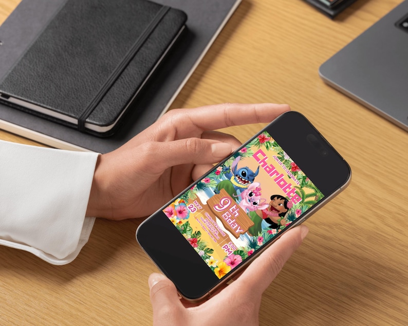May include: A smartphone displays a colorful invitation with the text "Charlotte 9th Bday" and cartoon characters. The invitation features a tropical floral border with Stitch, Angel, and Lilo. The phone is held by a person on a wooden surface.