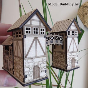 May include: Two wooden model building kits of medieval-style towers with stone and timber-framed walls, a bridge, and a tiled roof. The kits include pre-cut pieces and the text "Model Building Kit".
