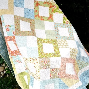 May include: A patchwork quilt with a white background and squares of various floral patterns in shades of blue, green, pink, and orange. The quilt is made with a variety of fabrics and textures, and the squares are arranged in a random pattern.