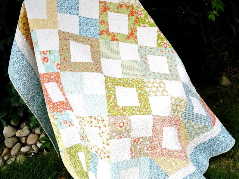 May include: A patchwork quilt with a white background and squares of various floral patterns in shades of blue, green, pink, and orange. The quilt is made with a variety of fabrics and textures, and the squares are arranged in a random pattern.
