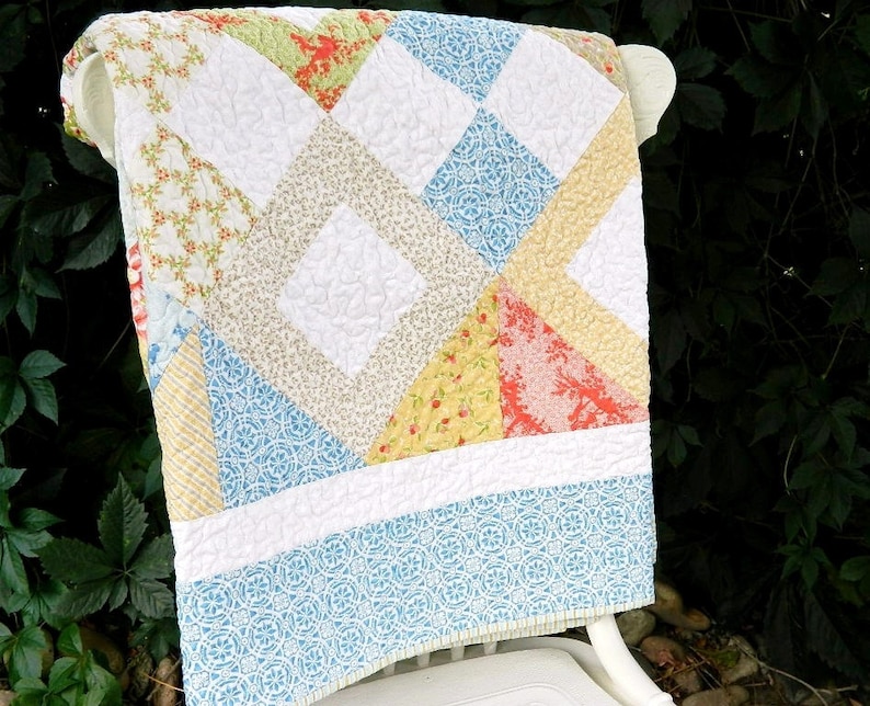 May include: A white, blue, yellow, and pink patchwork quilt with a diamond pattern. The quilt is folded and draped over a white chair.