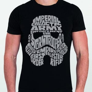 Puede incluir: Camiseta negra con un diseño de casco de Stormtrooper. El casco está formado por las palabras "Imperial Galactic Army", "Stormtrooper", "Empire", "Blaster" y "Rifle" en blanco. La camiseta es de cuello redondo.