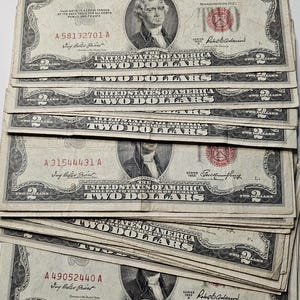May include: A stack of ten $2 bills, all from the 1953 series. The bills are in good condition and have a red seal and signature. The bills feature a portrait of Thomas Jefferson and the words "United States of America" and "Two Dollars".