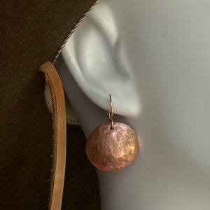 May include: A pair of hammered copper earrings with a round shape and a textured surface. The earrings are hanging from a simple wire hook.