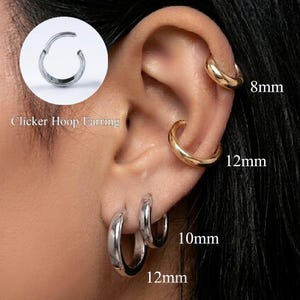 Può includere: Un set di orecchini a cerchio tipo clicker in tonalità oro e argento, mostrati su un orecchio. Gli orecchini sono etichettati con le misure 8mm, 10mm e 12mm. Il design presenta una banda metallica circolare liscia che si chiude con un clic sicuro.
