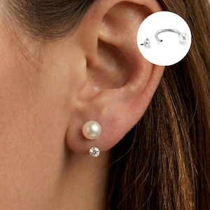 May include: A silver-toned earring set featuring a round white pearl stud and a small clear crystal stud worn on the earlobe. An inset circular graphic displays a silver-toned horseshoe-shaped earring with a pearl at one end and a crystal at the other.
