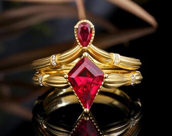 May include: A gold ring set with two red ruby gemstones. The larger ruby is a square cut and the smaller ruby is a pear shape. The ring is accented with small diamonds.