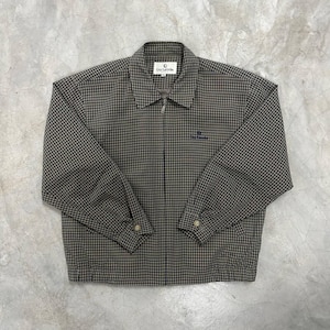 Peut inclure: Veste à carreaux marron et noir avec fermeture éclair complète. La veste a un col et des poignets boutonnés. Le logo de la marque "Guy Laroche" est visible sur la poitrine et le col. La veste est posée à plat sur une surface grise.