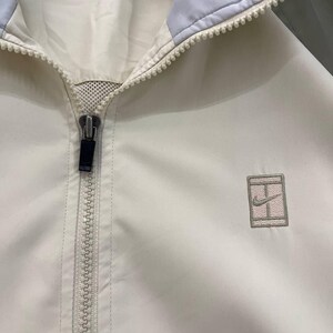 Peut inclure: Veste de sport cr&egrave;me avec un col bleu clair et une fermeture &eacute;clair compl&egrave;te. La veste pr&eacute;sente un petit logo brod&eacute; sur la poitrine. La veste est faite d'un mat&eacute;riau l&eacute;ger.