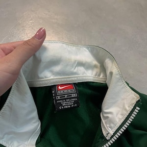 May include: Green and white Nike Team jacket with a full zipper. The jacket has a white collar and a tag that reads "Made in Sri Lanka" and "Clima-Fit". The jacket is a size small.