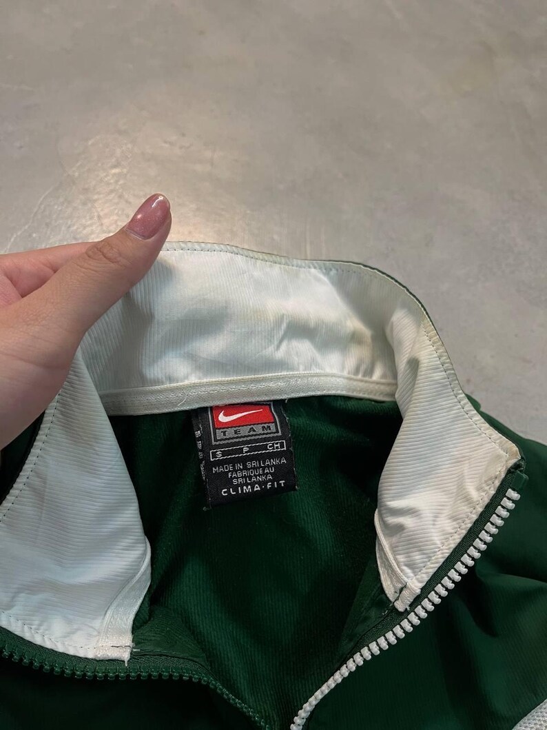 May include: Green and white Nike Team jacket with a full zipper. The jacket has a white collar and a tag that reads "Made in Sri Lanka" and "Clima-Fit". The jacket is a size small.