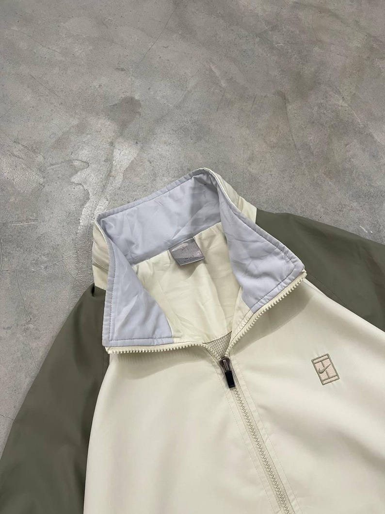 Peut inclure: Veste zipp&eacute;e cr&egrave;me avec col bleu clair et manches vert olive. La veste pr&eacute;sente un petit logo sur la poitrine et une fermeture &eacute;clair compl&egrave;te. La veste est faite d'un mat&eacute;riau l&eacute;ger.