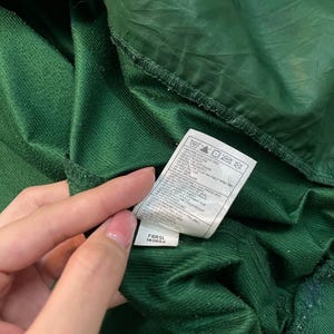 May include: Close-up of a dark green garment with a tag. The tag displays care instructions and the codes F6BSL and 14069X. The fabric has a textured, corduroy-like appearance.