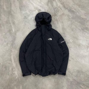 May include: A white ceramic mug with a black handle and the text "But First, Coffee" in a bold, black font. The mug is set against a blurred background, highlighting its clean design.