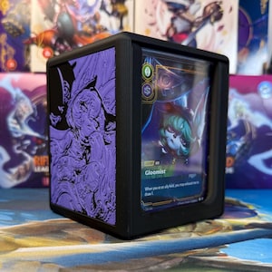 May include: Black card storage box with a purple embossed design. The box contains a card featuring a character illustration and the name "Gloomist". The box is designed for storing and displaying trading cards.