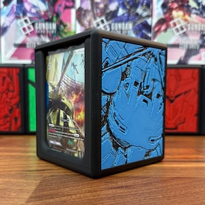 May include: Black card storage box with a blue embossed design on one side. The box holds a trading card with a green and yellow illustration. Other boxes are visible in the background.
