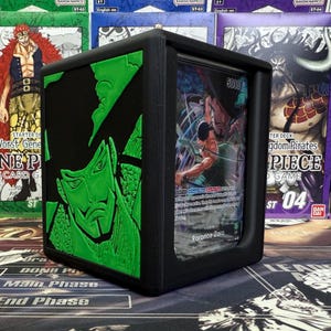 May include: Black card storage box with a green embossed character design on the side. The box holds trading cards, with one card visible featuring a character illustration. The background includes other card game boxes.