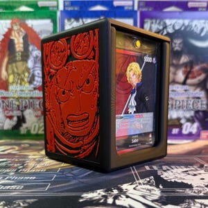 May include: Black and red card holder with a red embossed character design. The holder displays a card with a blonde-haired character and the text "Sabo". Other card packs are visible in the background.