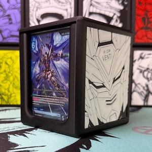 Puede incluir: Una caja de presentación negra impresa en 3D que contiene una carta coleccionable de Strike Freedom Gundam. El panel lateral presenta un diseño de cara mecánica blanca en relieve con el texto X-20A VENTI. La carta muestra un robot azul.
