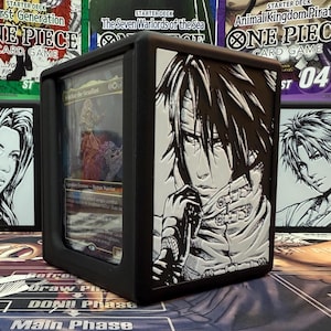 May include: Black card case with a clear front panel, featuring a detailed anime-style illustration in black and white. The case holds a trading card. The background includes One Piece and other card game starter decks.