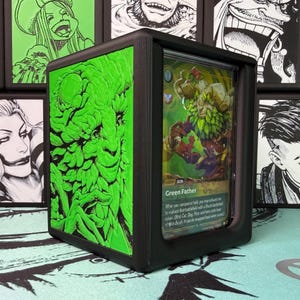 May include: A black 3D-printed display case featuring a vibrant green side panel with an embossed illustration of a leafy creature. The front window holds a collectible trading card titled Green Father, displaying a character with green foliage.