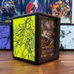 May include: Black card holder with a yellow and black illustration of a woman in armor. The holder displays a trading card with the text "Radiant Dawn". Other card holders are visible in the background.