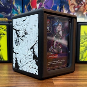 May include: Black card holder with a clear front panel displaying a card with a female character illustration. The holder has a white embossed design on one side. The card reads "Loose Cannon".