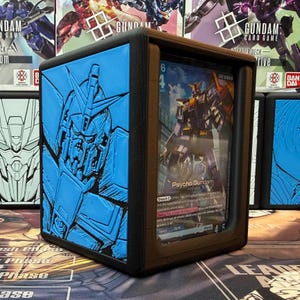 May include: A black and blue card holder featuring a blue embossed Gundam design on the side. The holder displays a card with a Gundam illustration and the text "Psycho Gundam". The holder is designed to protect trading cards.