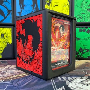 May include: Black deck box with a red and black image of a character from the anime One Piece. The box has a clear window to display a trading card featuring the character "Portgas D. Ace" with the text "Leader 5000".
