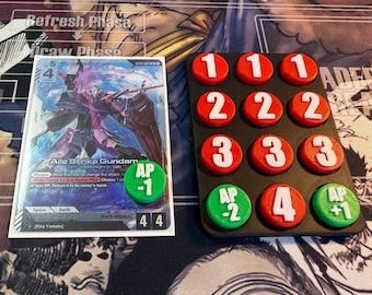 Puede incluir: Una carta de Digimon con un robot y el texto "Aile Strike Gundam", y un conjunto de fichas de juego rojas y verdes con los números 1-4. Las fichas están en una bandeja negra. La carta tiene el texto "Refresh Phase" y "Draw Phase".