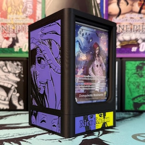 May include: Black card display case with purple and yellow accents. The case features a card with the text "Donquixote Rosinante" and "Nico Robin". The case has a black frame and is designed to hold trading cards.