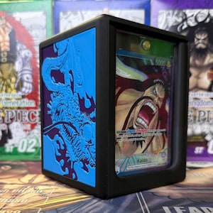 May include: Black card display case with a blue dragon design. The case holds a trading card featuring a character with the text "Kaido". The card is visible through a clear front panel. The case is designed to protect and showcase collectible cards.